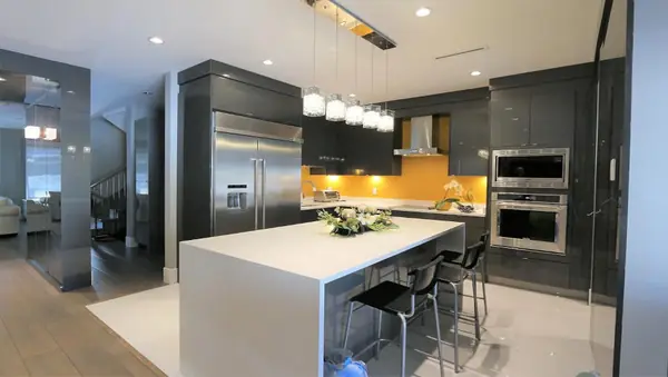 Dark kitchen with waterfall island, amber backsplash and wall ovens